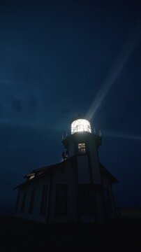 Vertical Screen: Foggy night lighthouse with bright rotating beam illuminating coastal air near Mendocino, California, USA creating cinematic dramatic lighting