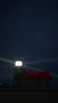 Vertical Screen: Night coastal scene with lighthouse beam spreading through fog in vertical composition near Mendocino, California, USA creating cinematic ocean atmosphere