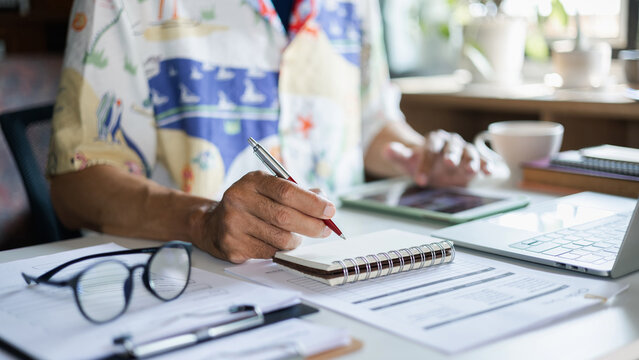 close up shot, casual man working at home via laptop and tablet checking note in calendar pad with documents to start online business, e-commerce