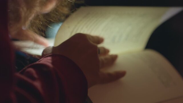 Closeup hands turning pages at night, curlyhaired writer flips journal under soft city bokeh and lamp glow, textured cover and inked margins, reflective solitude and gentle gestures.