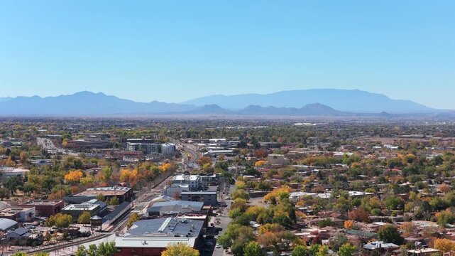 A rising drone shot captures the Santa Fe cityscape with the historic railyard area on the left. The footage highlights unique Southwest architecture and urban layout under a clear blue sky.