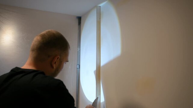 Worker putty wall with a spatula to repair surface imperfections. Interior renovation process showing smoothing and preparation of wall before painting in a home improvement project