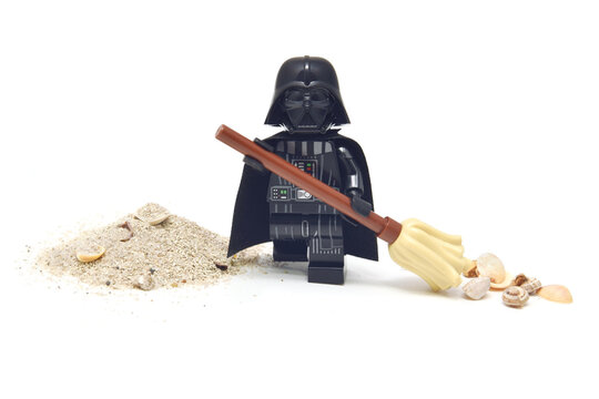 Lego minifigure of peaceful Darth Vader from Star Wars is cleaning a sand from seashell isolated on white. Editorial illustrative image of stop war concept.