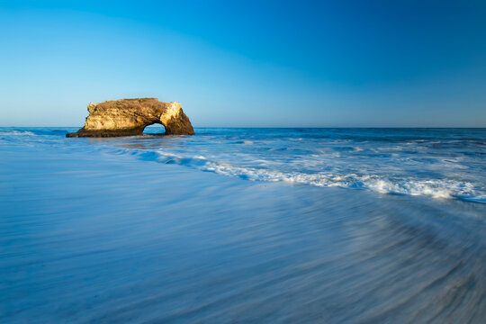 Natural Rock Arch at Santa Cruz Seaside with Motion Blur Waves and Clear Blue Sky