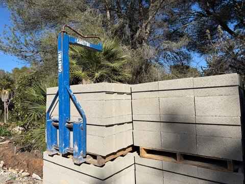 Santa ponsa, spain, march 30, 2026 grestal cinder block grabber lifting a pallet of concrete blocks on a construction site for new building