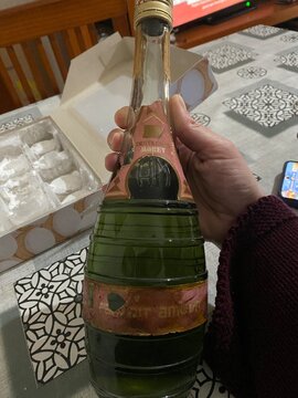 El puerto de santa maria, spain, january 2, 2026 hand holding old destilerias morey liqueur bottle on a patterned tablecloth, green glass and worn pink label
