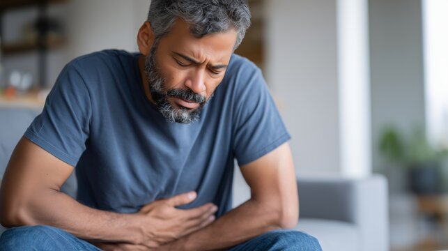 Man with stomach pain at home. Abdominal pain and digestive problem concept. Adult holding belly with cramps. Gastrointestinal illness and discomfort. Healthcare theme.