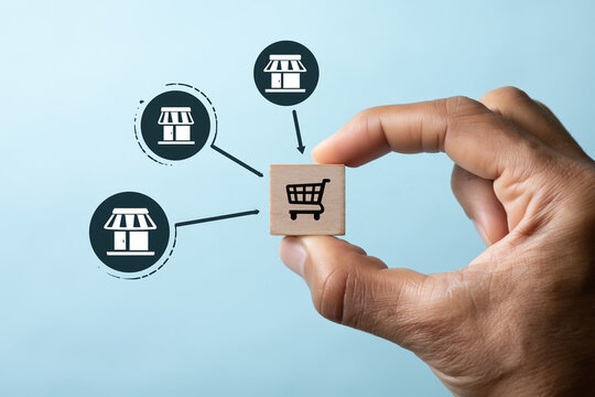 A hand holds a wooden cube featuring a shopping cart icon linked to multiple store symbols indicating a retail network