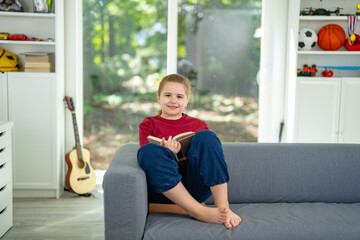Kid reading a book at home. Child enjoying storybook in cozy room. Little boy reading books in...