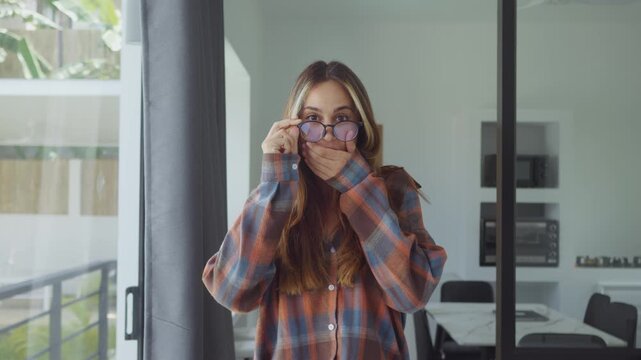 shocked woman adjusting glasses reacting to unexpected news in bright modern apartment interior. shocked woman covering mouth in disbelief showing strong surprise and emotional reaction indoors