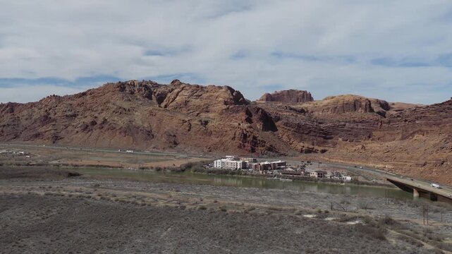US 191 Colorado River Bridge near Moab Utah spanning the Colorado River beside Fairfield Inn and Suites Moab below Entrada Sandstone formations in arid canyon terrain, drone oblique glide forward