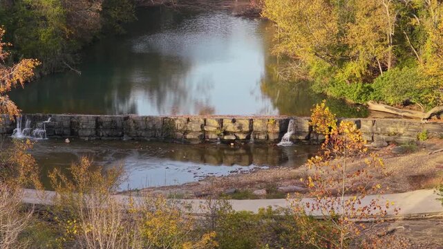 Old stone dam with small waterfalls along forest river at Natural Dam Arkansas autumn landscape, drone telephoto establishing