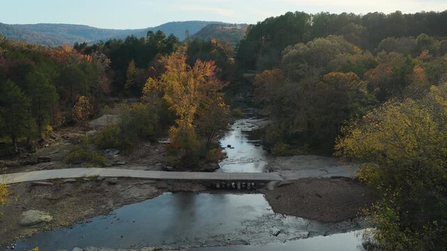 River crossing bridge with small waterfall in autumn forest, Natural Dam Arkansas, drone dolly establish