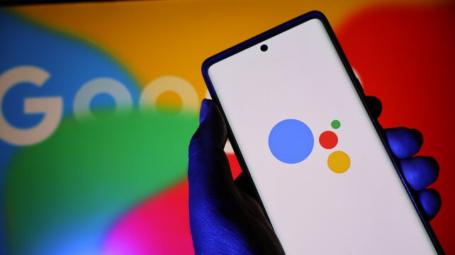 Hand holding smartphone with google assistant app on screen in front of colorful background