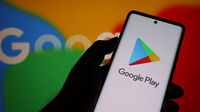 Hand holding smartphone with google play app on screen in front of google logo background