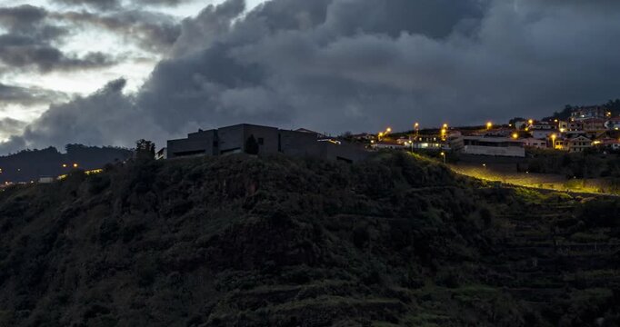 Calheta city hillside illuminated at dusk with dark clouds above. Aerial Hyperlapse
