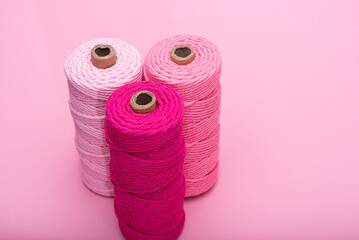 Three spools of thread in various shades of pink, arranged on a light pink background.