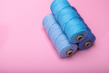 Three spools of woven cord in different shades of blue, displayed on a bright pink backdrop.