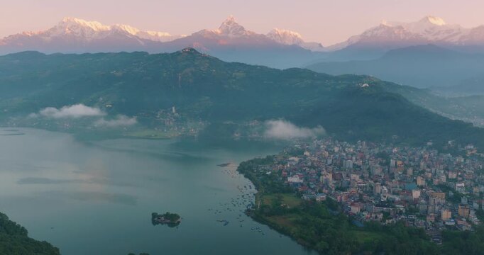 Aerial shot of calm Phewa Lake Pokhara Nepal at tranquil dawn with Tal Barahi Temple and Lakeside area beneath Annapurna and Machhapuchhre Himalayan peaks.