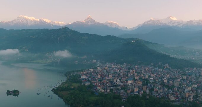 Aerial shot of golden sunrise over Pokhara Phewa Lake Nepal with Tal Barahi Temple at the center surrounded by lush green hills and Annapurna and Machhapuchhre peaks in lake.
