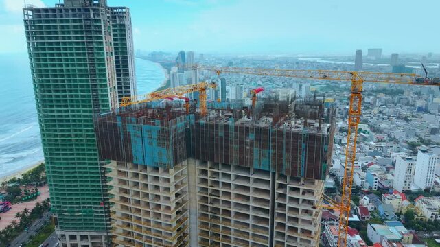 Urban skyline with cranes and high rise construction near ocean in Da Nang Vietnam. Urban expansion concept shows infrastructure growth modern city planning and coastal megacity lifestyle.