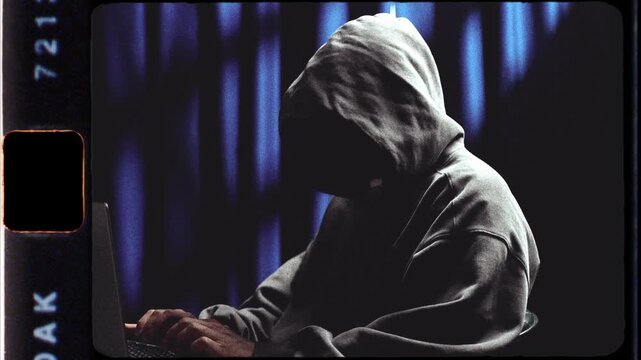 Anonymous hooded hacker working on laptop computer