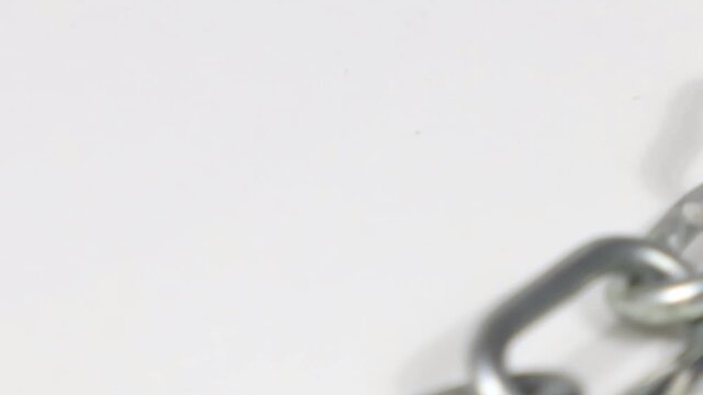 A steel chain moving through view, on a white background. On a plate spinning.
