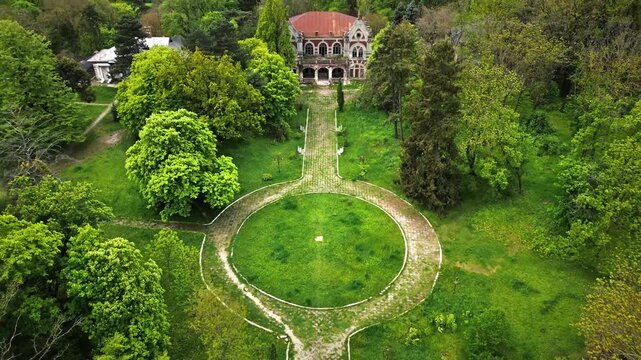 Aerial drone cinematic shot of abandoned vintage manor house mansion ruins in lush green forest park.