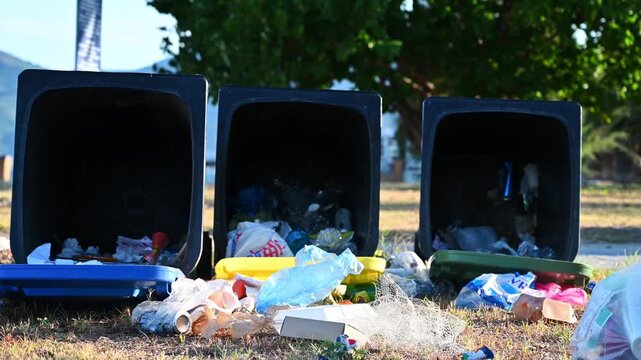 Overflowing waste bins with spilled trash in park area showing pollution and environment management.