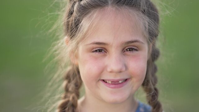 Smiling girl with braid in hair smiling in outdoor green field portrait child face showing happy expression and missing tooth hair flyaway natural smile joyful grin playful look and innocent charm