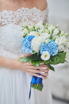 Hands of a bride in a white lace dress holding a wedding bouquet of roses, side view