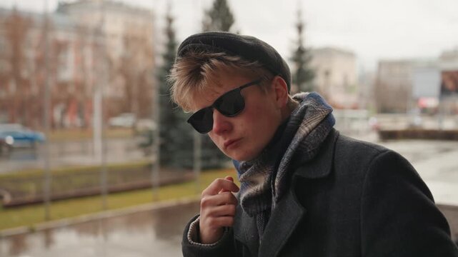 White creator in rainy balcony closeup, introspective portrait of white male creator touching chin and scanning street, beret and scarf detail, soft bokeh and muted urban backdrop, editorial mood