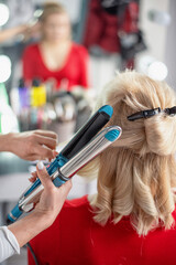 Fototapeta premium Hairdresser styling blonde hair with a curling iron in a salon setting
