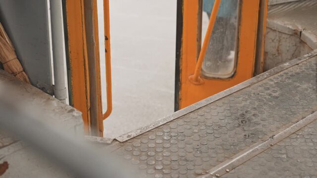 Person in teal jacket boarding orange train door, creator filming candid urban commute, metal steps, worn platform, overcast light, slow steady movement, intimate streetlevel moment