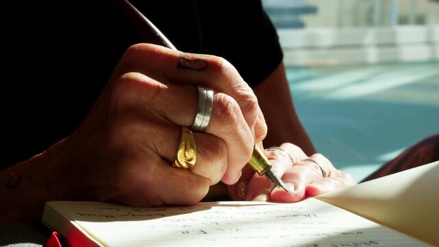 Extreme close-up of mature hands elegantly writing with a classic fountain pen in a notebook. Atmospheric lighting highlighting the texture of paper and the art of traditional journaling