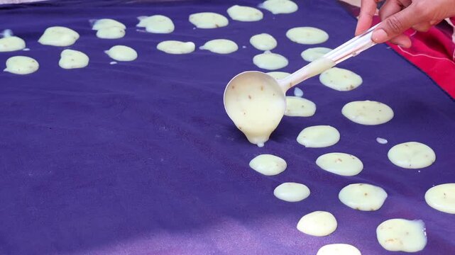 Traditional preparation of homemade rice papadums being spread onto a cloth for sun drying.