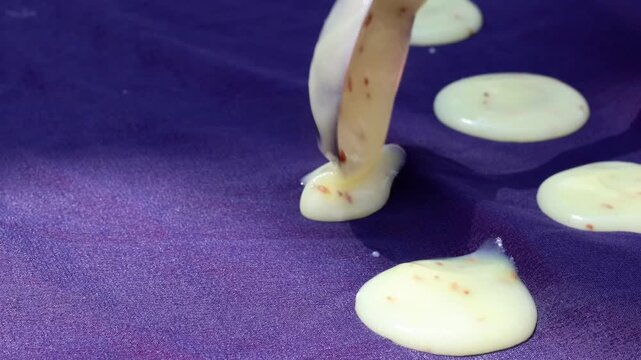 Close up view of a person pouring small rounds of white batter to make authentic sun-dried papads.