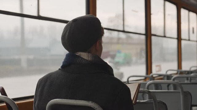 White creator on tram reading book and studying pages, window city view and muted palette young white student and writer absorbs urban scene, pen and notebook nearby, slow motion of commute inspires
