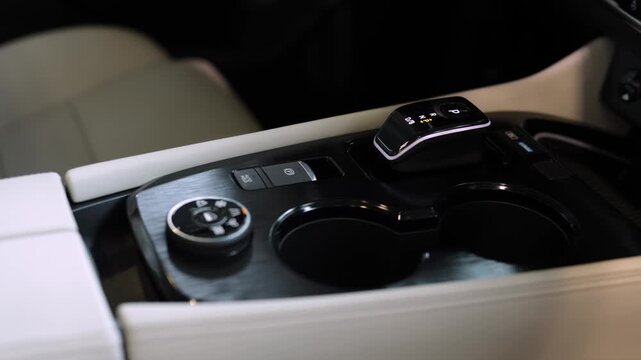 Modern vehicle interior featuring sleek center console with gear shifter, cup holders, and control buttons, showcasing a luxurious design aesthetic in a contemporary car