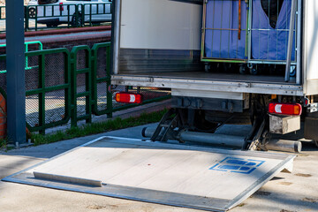 Delivery truck with hydraulic tail lift lowered for unloading goods, metal roll cage container inside the vehicle, city logistics, freight transport and courier delivery service. © Adam