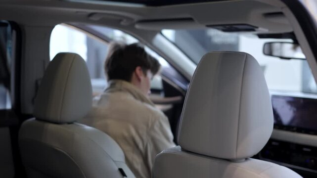 Man entering new vehicle in car showroom, choosing modern automobile. Car buying concept.

