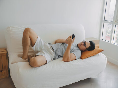 Asian man focus on the phone while relaxed on the sofa.