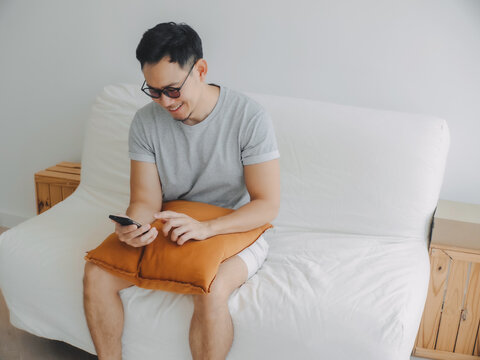 Asian man sitting comfortably on couch composing digital message