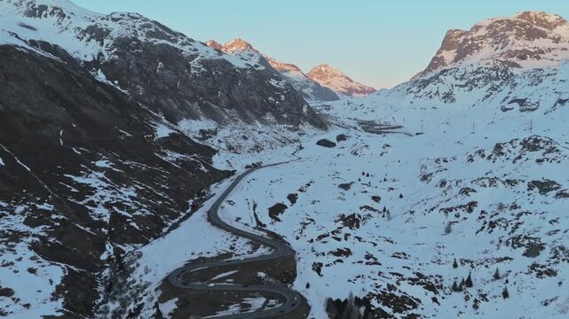 Aerial view of a winding road cutting through the snow-covered Julierpass valley with mountains towering in the background, Julierpass, Grisons, Switzerland.