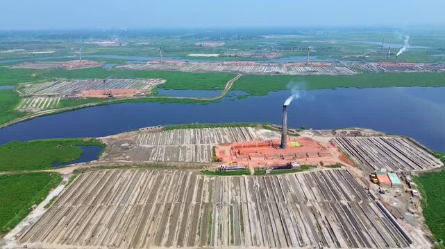 Aerial view of brick factories with long rows of bricks, chimneys expelling smoke, and a river flowing through the area, Dhaka, Dhaka Division, Bangladesh.