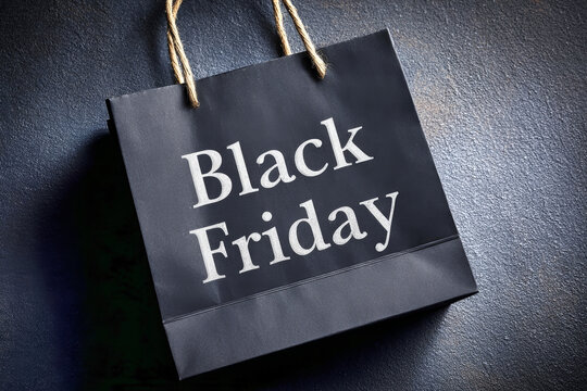 The black paper shopping bag with Black Friday text sits against a dark gray backdrop, signifying the start of a popular sale event for shoppers