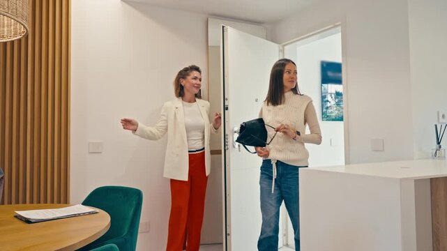 Real estate agent show modern apartment to potential female buyer. Happy woman client entering property for sale or rent, looking around and smiling.Property tour indoors, home buying  concept.