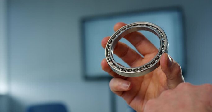 Hand holding steel ball bearing close up in engineering office or industrial laboratory environment