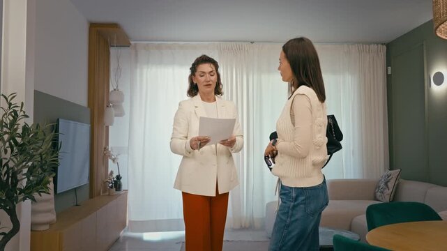 Real estate agent present apartment to buyer,explaine property features and discuss purchase agreement inside living room. Property viewing indoors, house market, investment,lifestyle decision concept