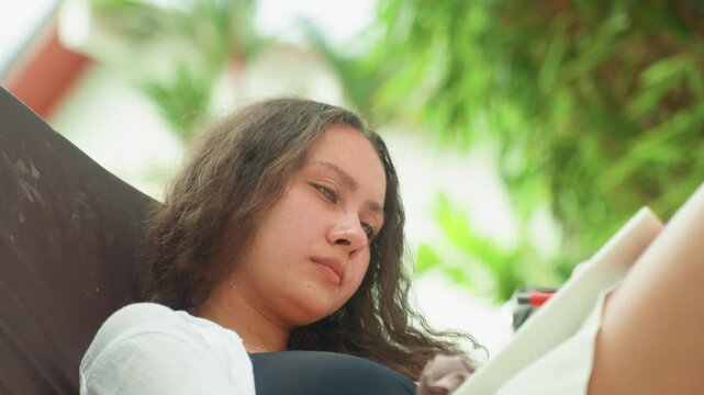 Woman journaling peacefully. Female enjoying leisure by recording thoughts in natural surroundings. Woman on vacation engaging in reflective writing while seated comfortably among lush plants